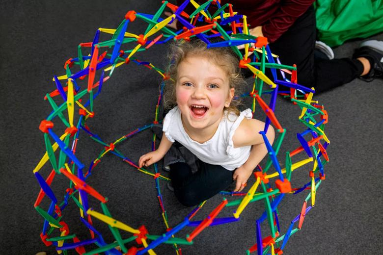 A child smiles while surrounded by colorful toys on the floor