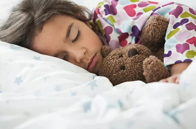 A child sleeping with a teddy bear.