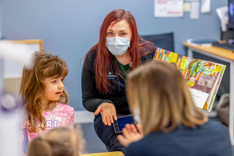 A caregiver in a mask talks with a small group of children