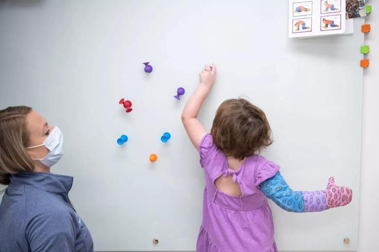 Little girl in a purple shirt grabs toys stuck to a wall