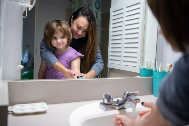 Little girl watches in the mirror as a woman washes her hand