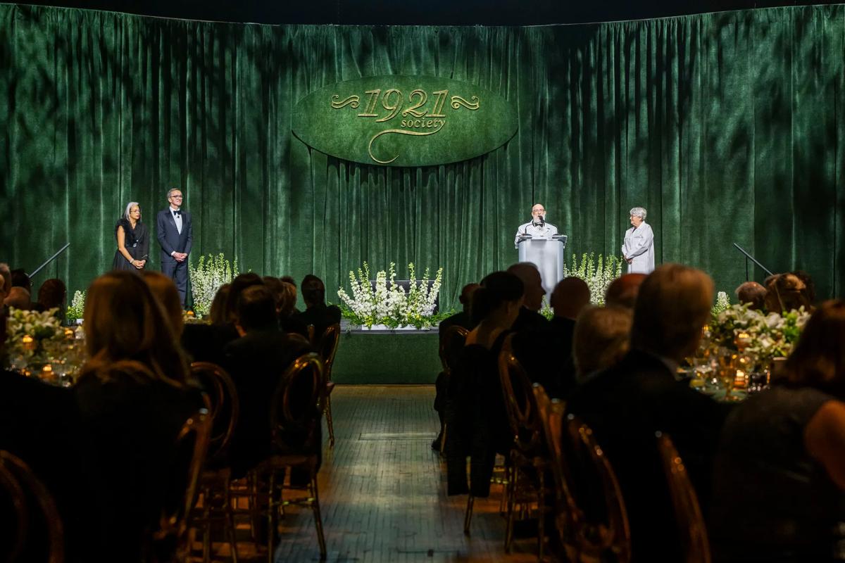 1921 Society event with person speaking on stage with Lara Kalafatis and Dr. Mihaljevic.
