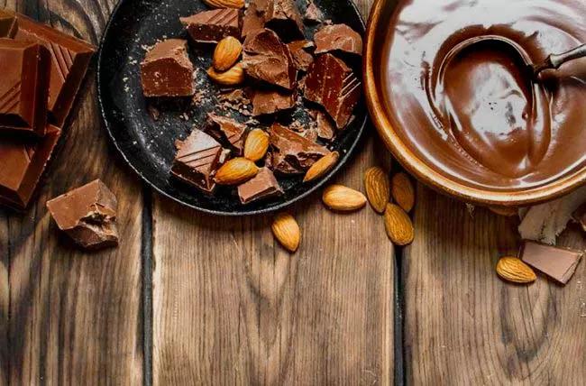 Dark chocolate and almonds on plate, with bowl of melted chocolate