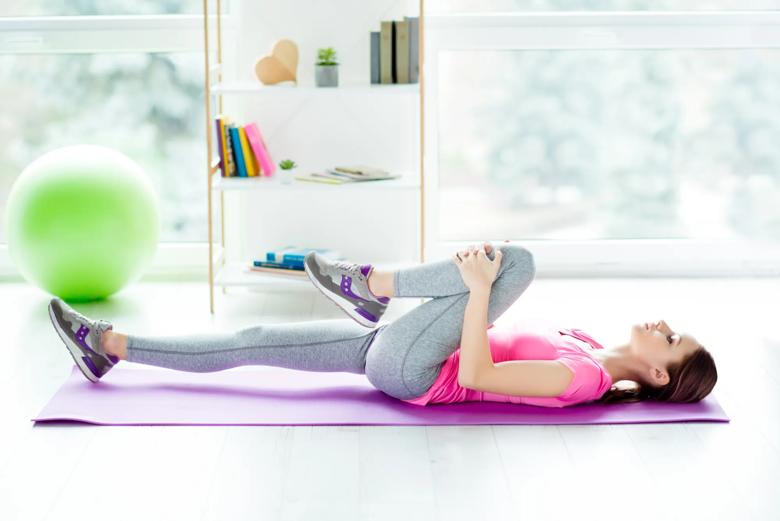 A person brings their knee up toward their chest while lying on a mat
