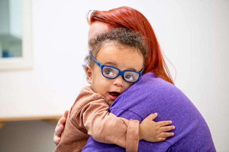 Little boy in blue glasses hugs an adult in a purple shirt