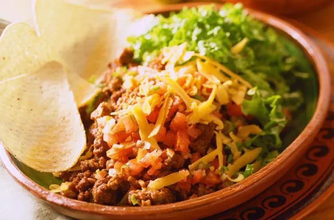 Bowl of taco salad, with rice, lettuce, cheese and tomatoes