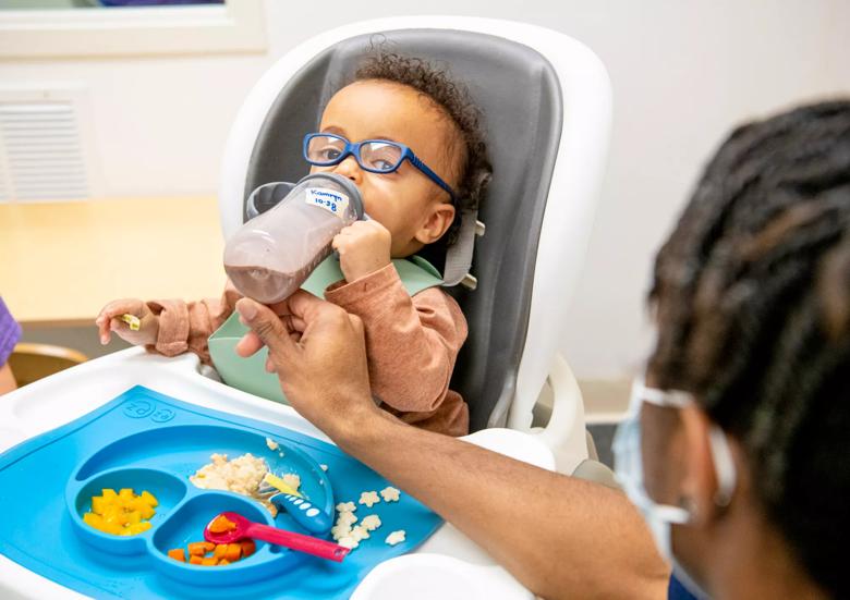 Little boy sits in a high chair while drinking from a sippy cup