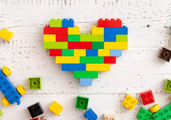 Multi-colored plastic cubes are scattered on a white wooden table. Creative building in the shape of a heart from a bright constructor. Early learning. Educational toys