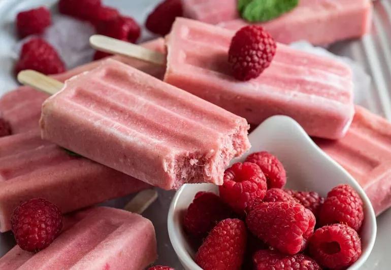 pineapple raspberry popsicles with a small bowl of raspberries