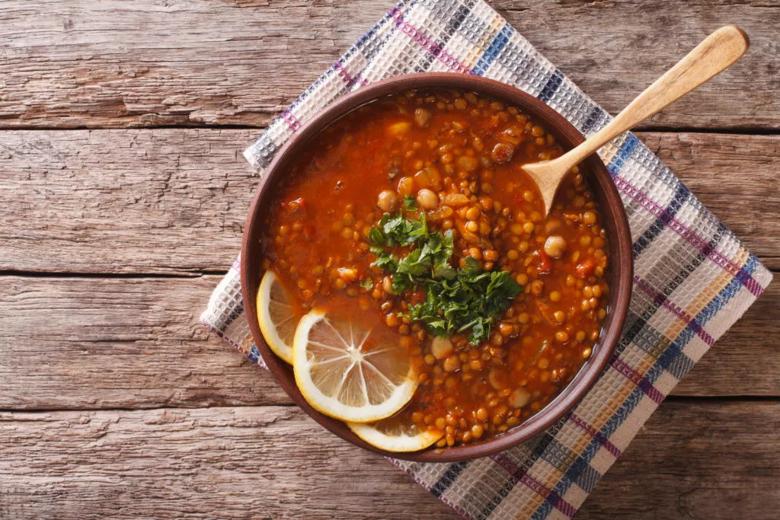 Tomato, chickpea and lentil soup in bowl on table with wooden spoon