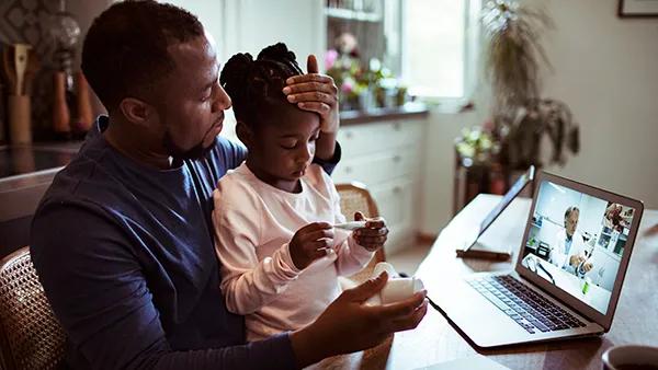 A parent with their child on a virtual visit on a laptop.
