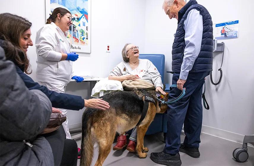 A woman sitting in a chair next to a man with a therapy dog and a Cleveland Clinic caregiver.