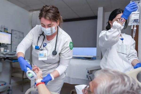 Two nurses assisting an older man laying in a hospital bed.