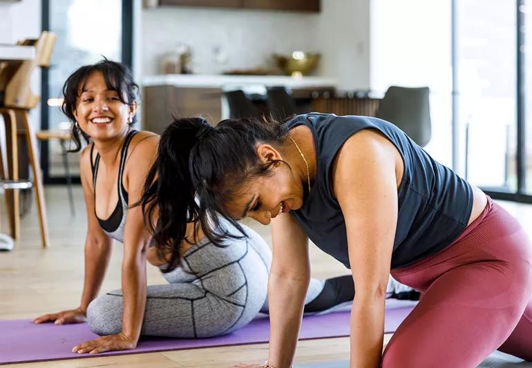 Two people performing yoga on the floor mats in their home.