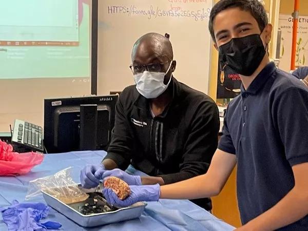 A student and a resident pose for a picture. The student is holding a brain.