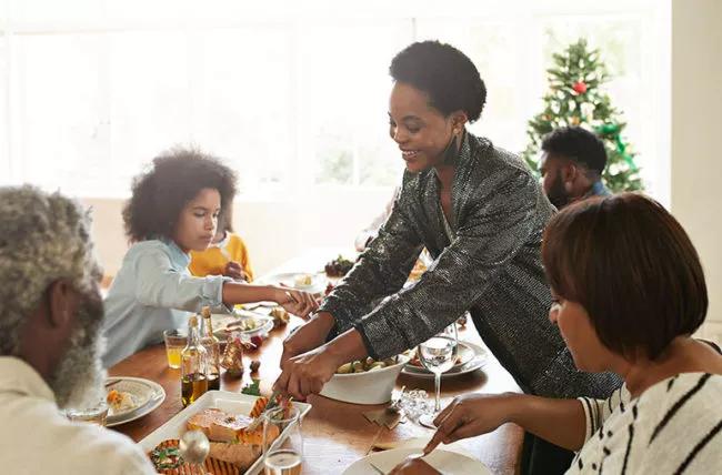 Woman serving food to her family at the dining room table.