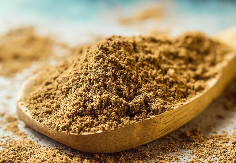 A close-up of a wooden spoon with a big pile of the brown spice cumin