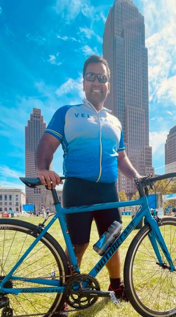 Amar Gupta, MD, wearing a VeloSano shirt, outside with his bike.