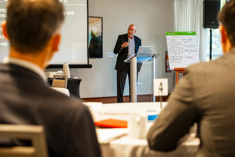 Man at a podium lecturing to men in business suits