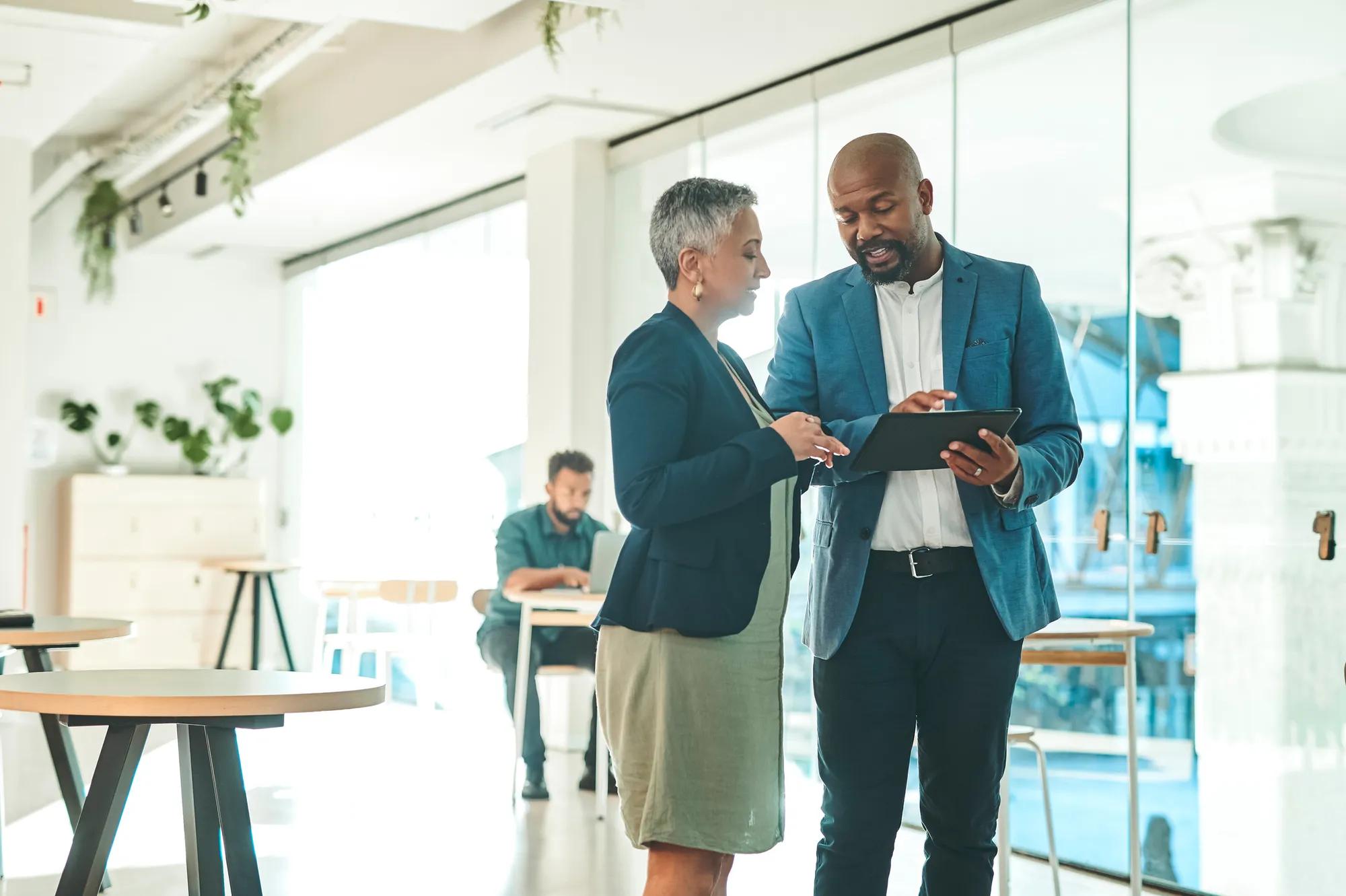 Two business professionals review information on a tablet in a modern office workspace.