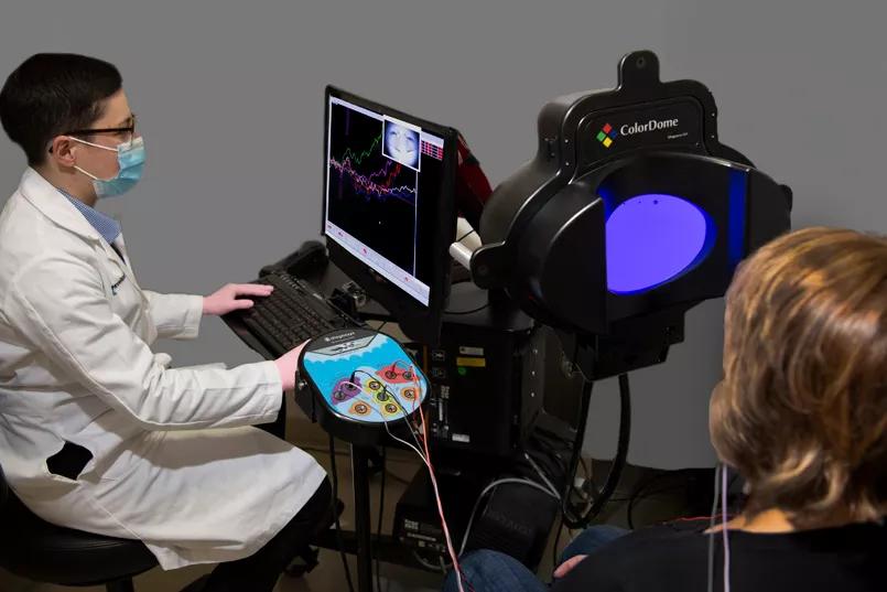 The patient looks at a purple screen while the doctor sits at a nearby computer