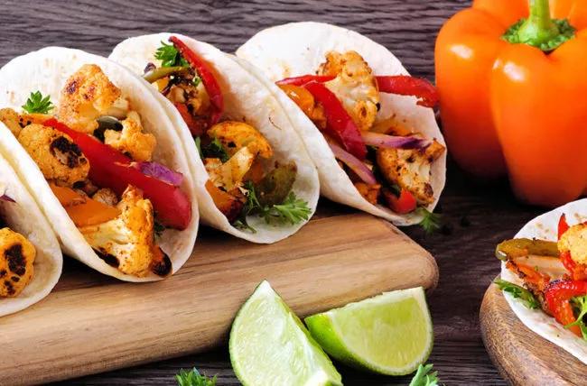 Roasted cauliflower soft tacos on cutting board, with limes on table