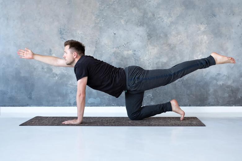 A person uses one hand and one knee to support themselves while lifting the opposite arm and leg