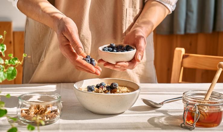 Person adding handful of blueberries to bowl of oatmeal