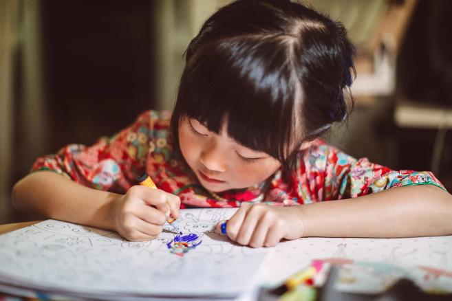 Child bent over coloring book, coloring with a marker