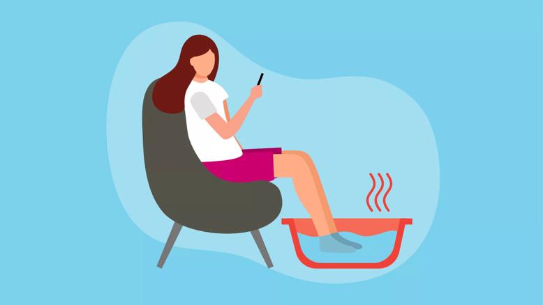 Person sitting in chair soaking feet in warm tub of water.