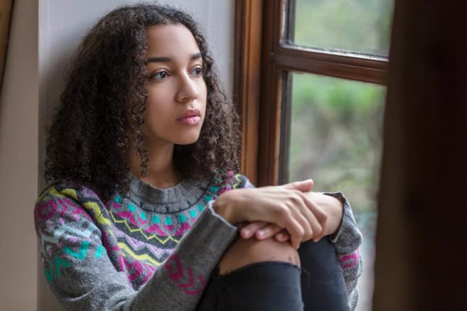 Teen sitting in window well staring out the window