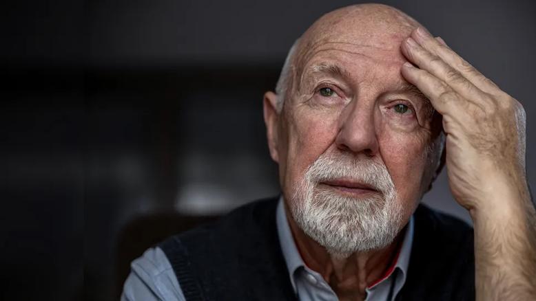 old man looking pensive with hand on forehead