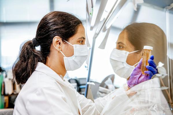 A woman in a lab coat and mask examines container.