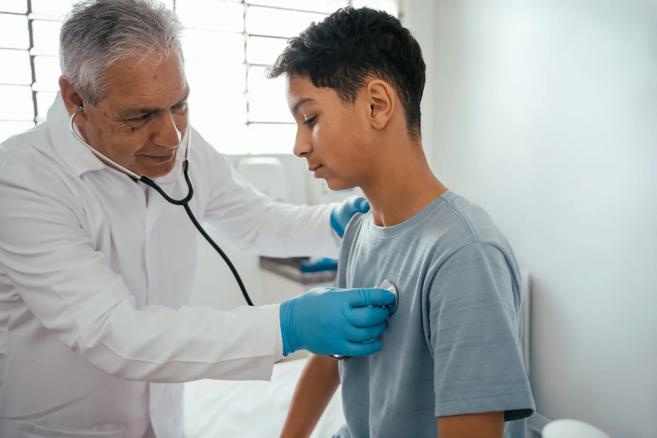 Doctor uses stethoscope to listen to chest of boy in clinic