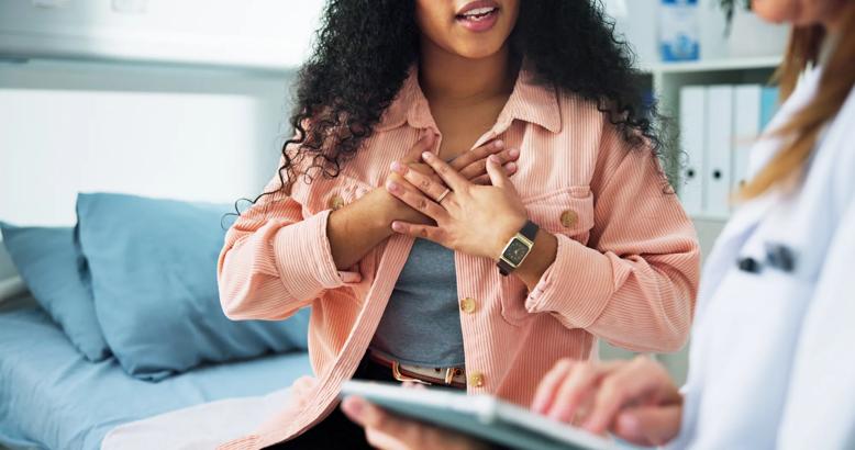 woman on a bed grasping her chest in front of a doctor