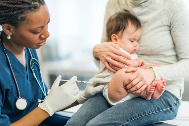 Caregiver holding a baby receiving a vaccination shot from a healthcare provider