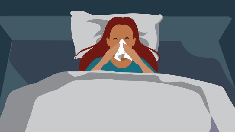 Person lying in bed at night blowing their nose with a tissue