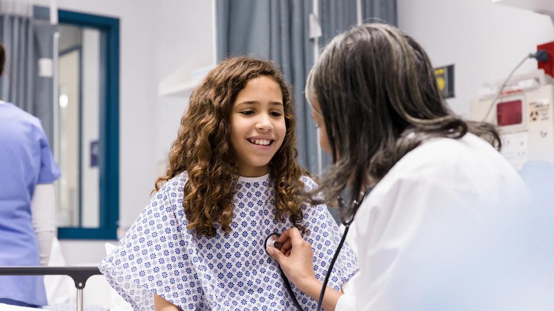 Adolescent patient sitting on hospital bed while provider uses stethoscope