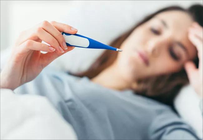 Sick woman lying in bed, examining a digital thermometer reading.