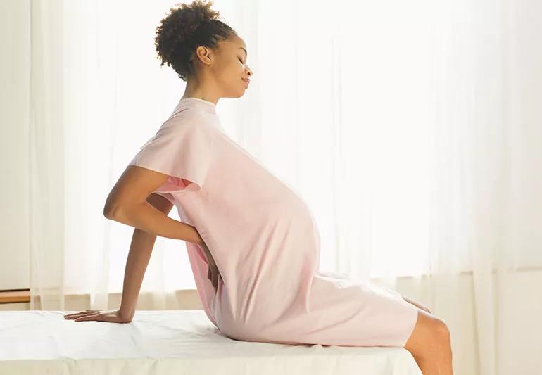 Pregnant woman with rheumatoid arthritis sitting up on bed.