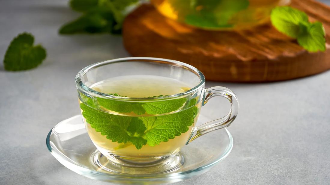 Glass mug of lemon balm tea with fresh lemon balm herb