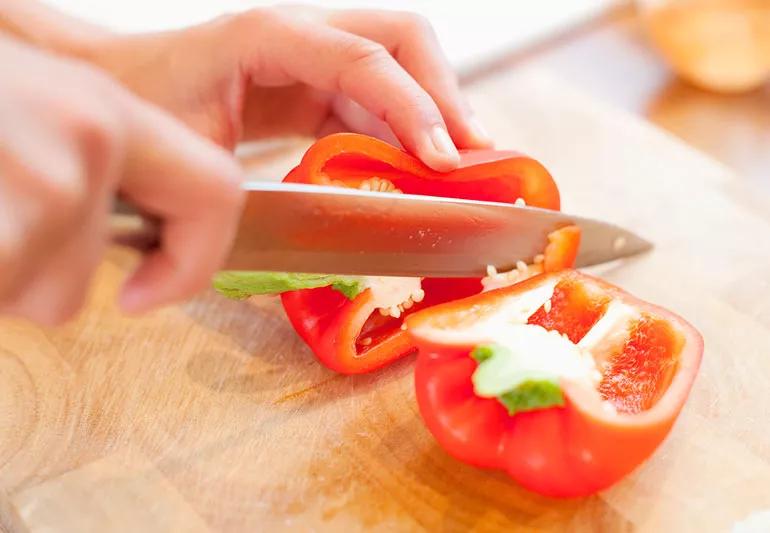 Person preparing a red bell pepper by slicing it up to eat.