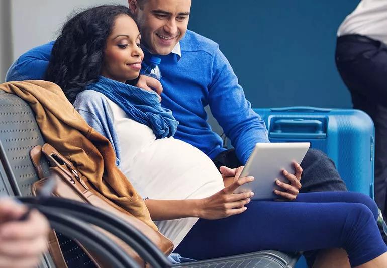 Pregnant woman and partner looking on ipad while waiting for flight at the airport.