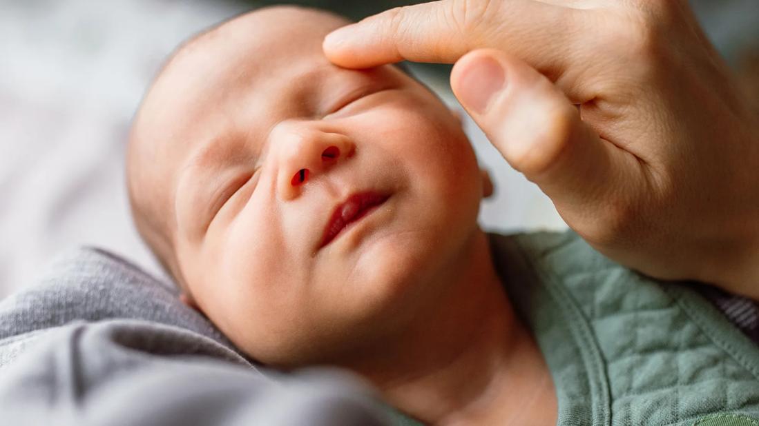 Face of sleeping newborn baby, face being lightly touched by caregiver hand