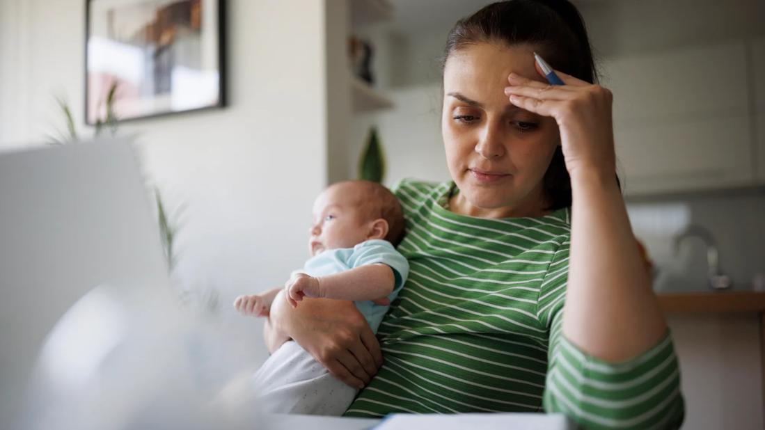 Caregiver holding newborn while also reviewing paperwork at home