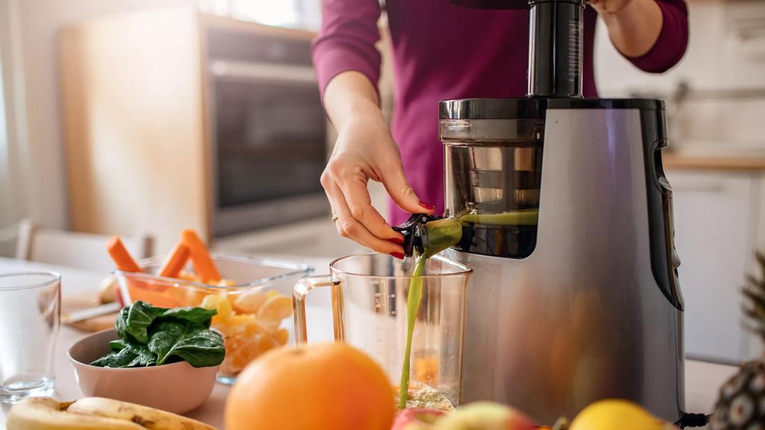 Juiced fruits and veggies dispensing from a juicer on counter in kitchen
