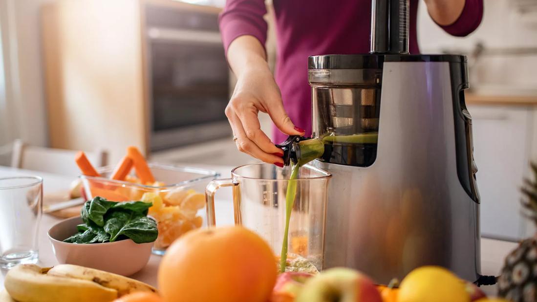 Juiced fruits and veggies dispensing from a juicer on counter in kitchen