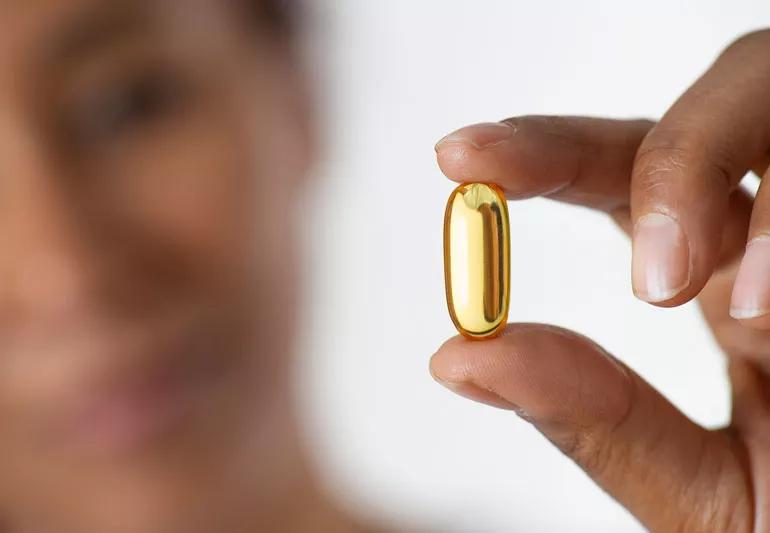 closeup of person holding vitamin d gel capsule between fingers.