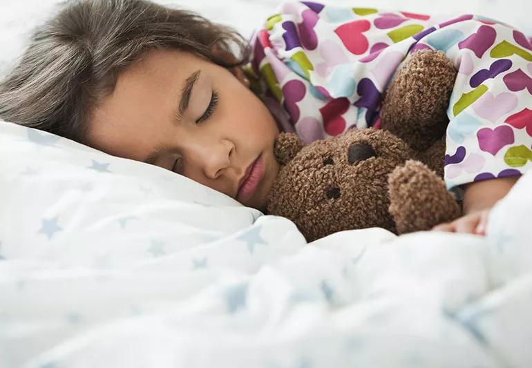 Child sleeping in bed holding teddy bear.