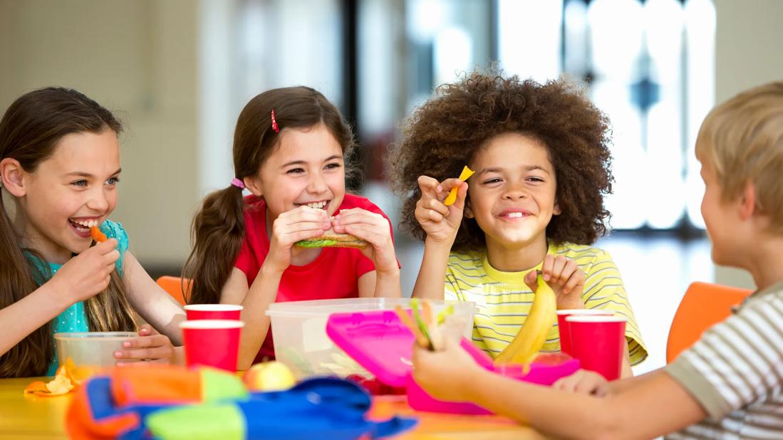 Happy elementary school kids smiling, eating lunches at table